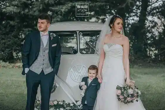 Wedding couple with page boy in front of white classic vehicle